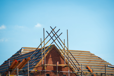 Construction site showing a partially finished roof with wooden beams and scaffolding against a blue sky.