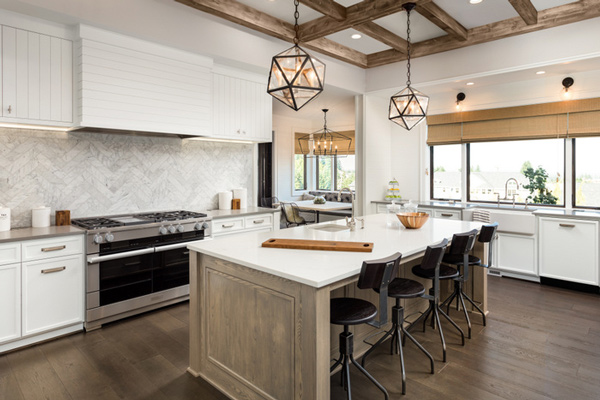 Modern kitchen with white cabinetry, a large island with a wooden countertop, and stylish pendant lighting, featuring a gas stove and a marble backsplash. Bright and airy design characteristic of contemporary interiors.