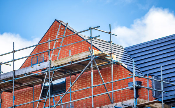 Building under construction with scaffolding, showcasing brickwork and roof details.