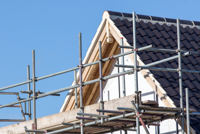 Roof construction with scaffolding against a clear blue sky, highlighting the roofing materials and structure.