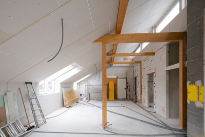 spacious interior view of a partially renovated attic with wooden beams and construction materials, featuring large windows and unfinished walls, ideal for home renovation projects