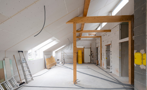 interior of a modern home under construction featuring exposed wooden beams, drywall, and electrical wiring, showcasing the open layout and natural light coming through the skylights