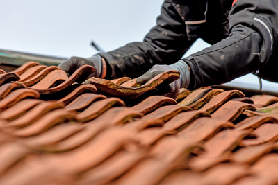 A worker carefully placing a clay tile on a roof, showcasing a close-up view of the textured tiles and the craft of roofing.