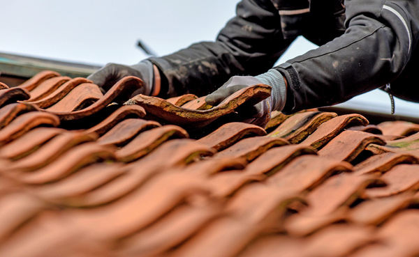 A worker carefully adjusts clay roof tiles while installing them on a roof.