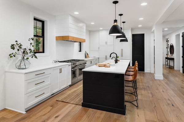 A modern kitchen featuring white cabinetry, a large central island with black accents, stylish bar stools, and pendant lighting, surrounded by natural wooden flooring and contemporary design elements. Ideal for home design inspiration and kitchen renovation.