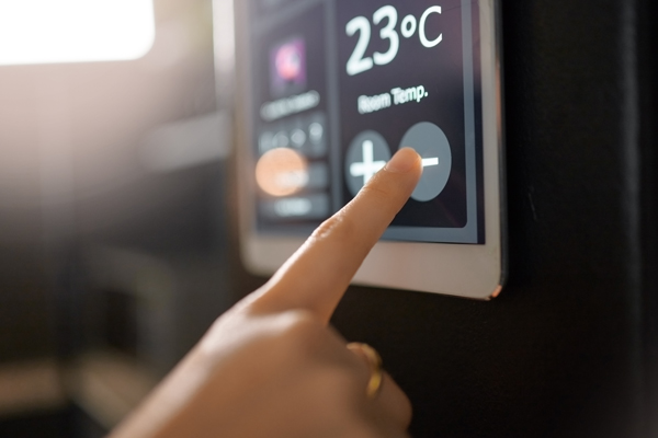 A hand adjusting the temperature on a digital thermostat displaying 23°C.