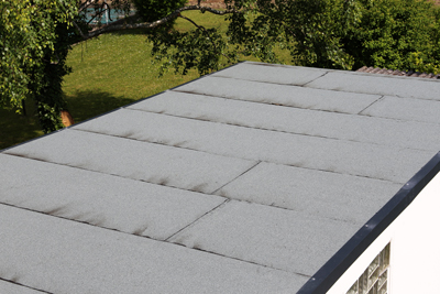 flat gray roofing material on a building with green trees in the background, showing clean and well-maintained surface