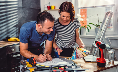 A couple discussing home improvement options at a cluttered table with tools and color swatches for DIY projects.