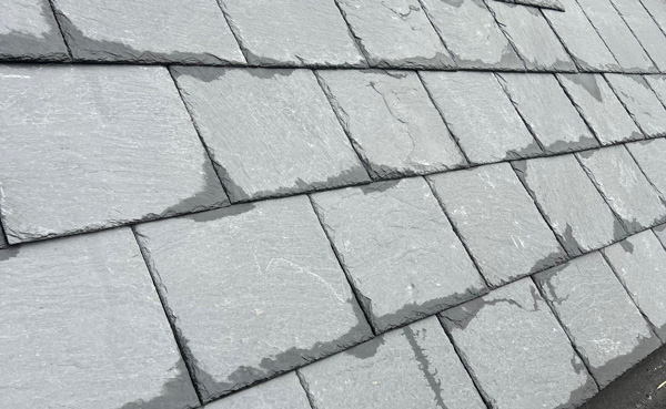 close-up view of a slate roof with slightly wet tiles, showcasing the texture and color variations of the gray slate materials