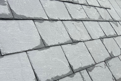 close-up of dark gray slate roofing tiles with wet surfaces reflecting light, showcasing texture and color variation