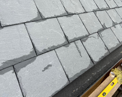 Slate roof tiles installed on a sloped surface, showing various shades of gray with some water droplets, emphasizing durability and quality roofing materials.